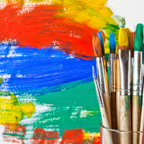 Yellow, red, blue and green paint on a canvas with paint brushes in a glass container in front.