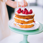 Layered sponge cake on a cake stand with child's hand dusting cake with icing sugar.